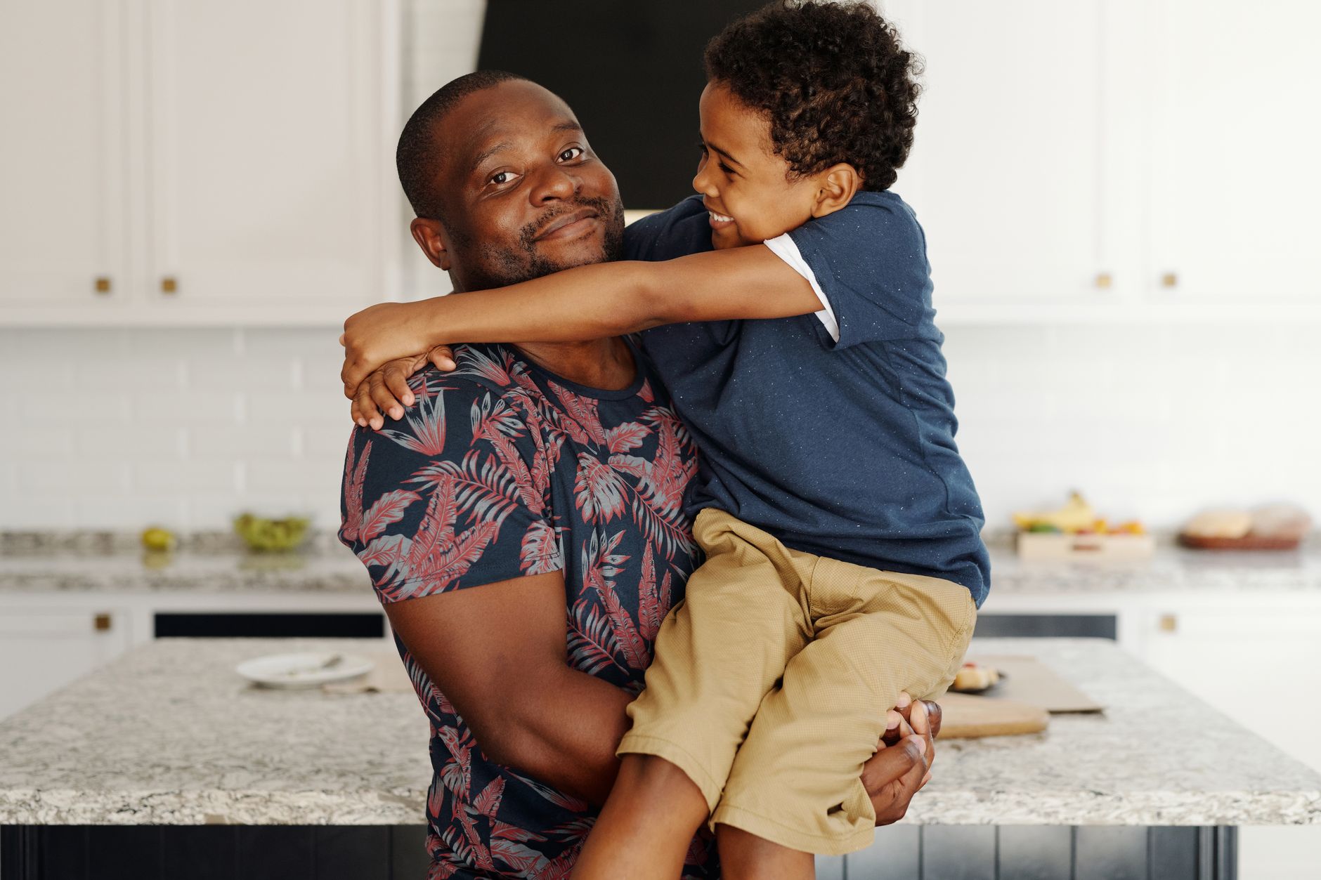 A man holding a smiling young boy in his arms in a kitchen.